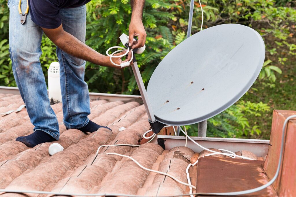 Worker installing satellite dish and antenna on roof top